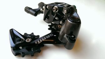 The X-SYNC pulley is larger and has profiled teeth like the chainring. The cage lock button sits beneath the clutch housing.