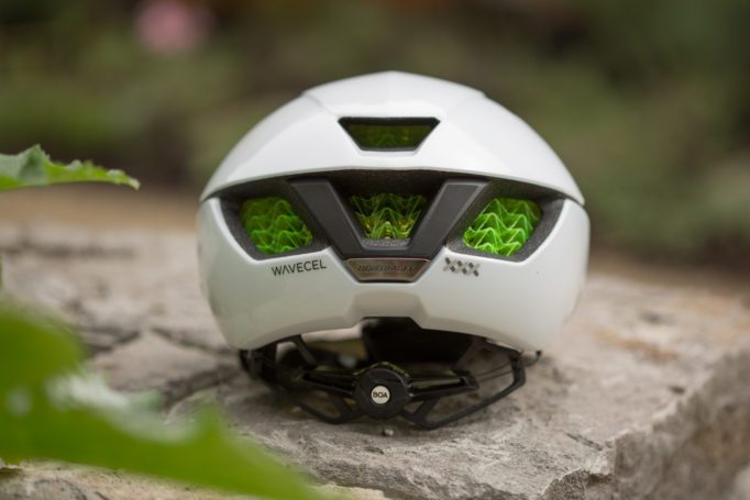 rear view of a white road bike helmet sitting on a stone planter with out of focus plants nearby.